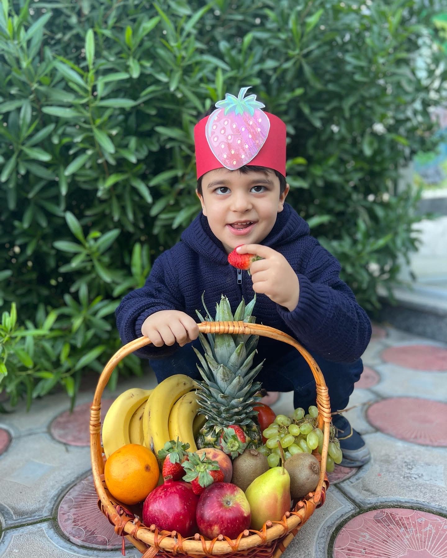 Sanny Kindergarten Student holding a basket of fruit and a hat.