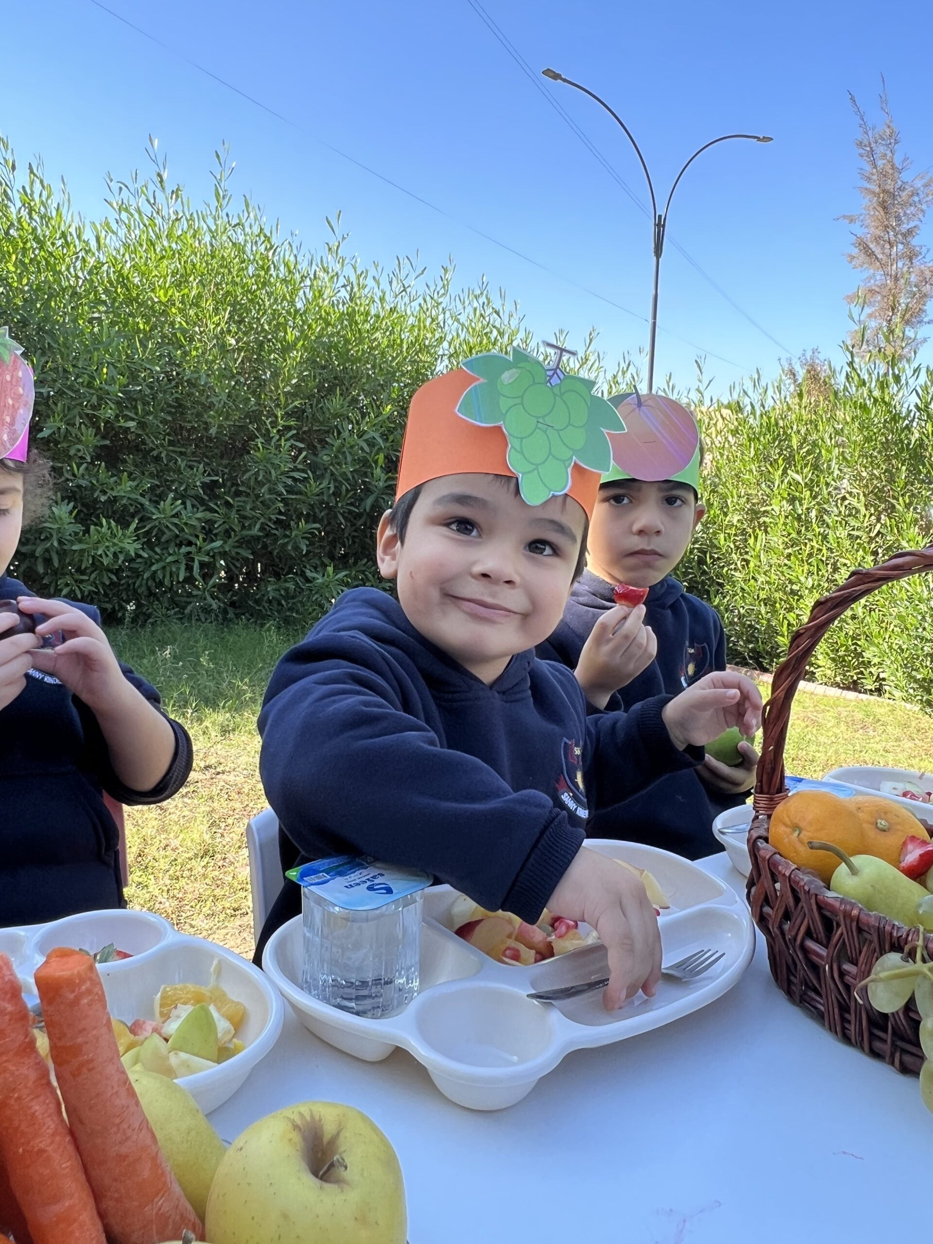 Sanny Kindergarten students sitting around a picnic table.sitting at a table eating fruit and vegetables.